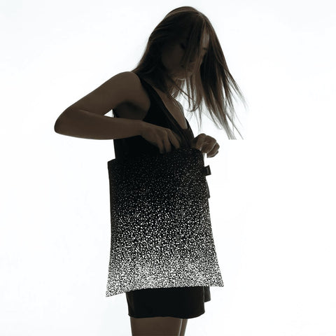1. Woman holding MARCH Reflective Tote SPLASH in lifestyle setting, showcasing reflective design