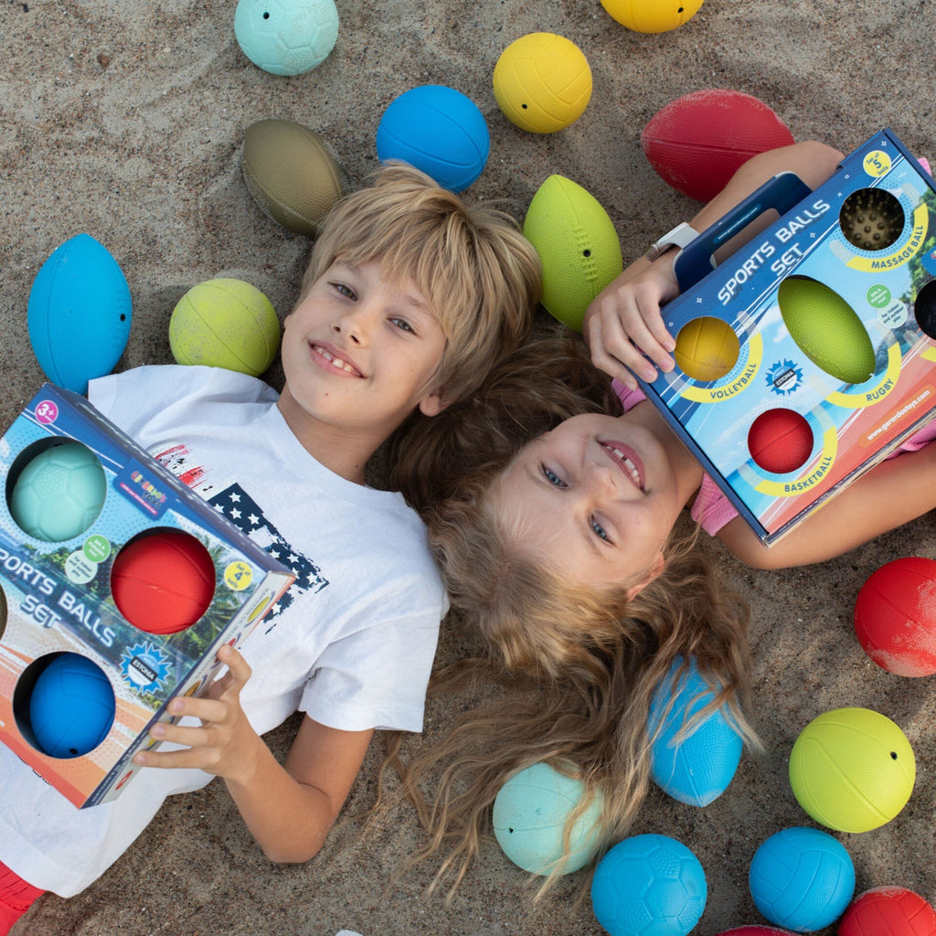 1. Two children lying on sand surrounded by colorful sports balls, each holding a Gerardo's Toys sports balls set box