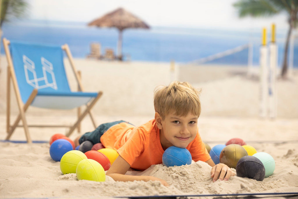 1. Boy lying on sandy beach surrounded by colorful Gerardo's Toys sports balls with ocean in background