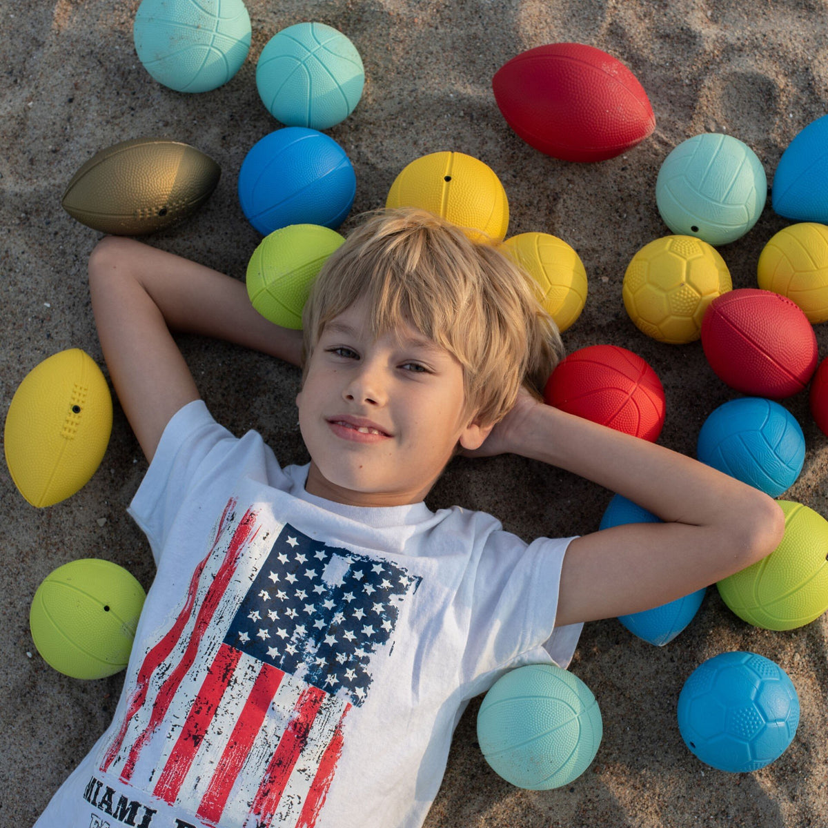 1. Boy lying on sand surrounded by colorful Gerardo's Toys sports balls