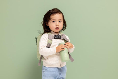 1. Child holding green dragon-themed bottle with backpack, light green background