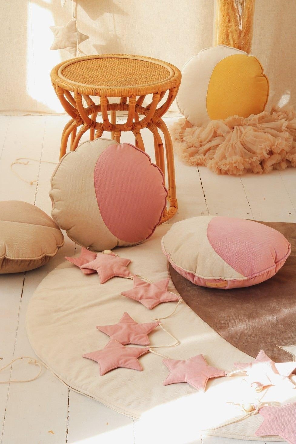 3. Soft pink star garland with round cushions and wicker stool in warm-toned room