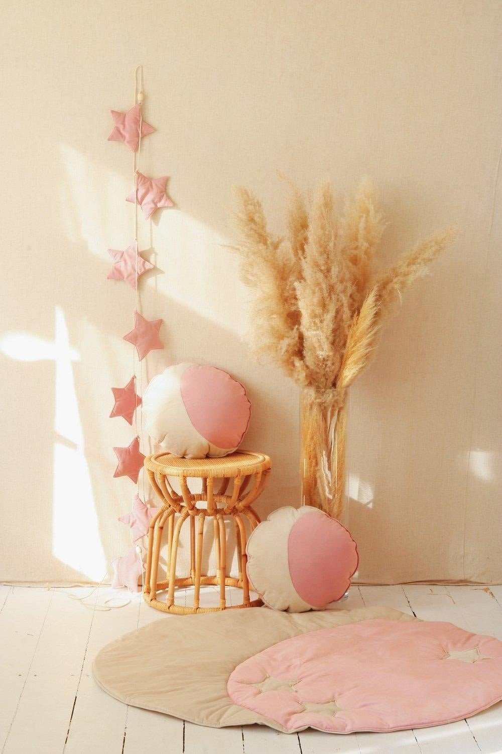 1. Soft pink star garland hanging on beige wall with round cushions and pampas grass in cozy room setting