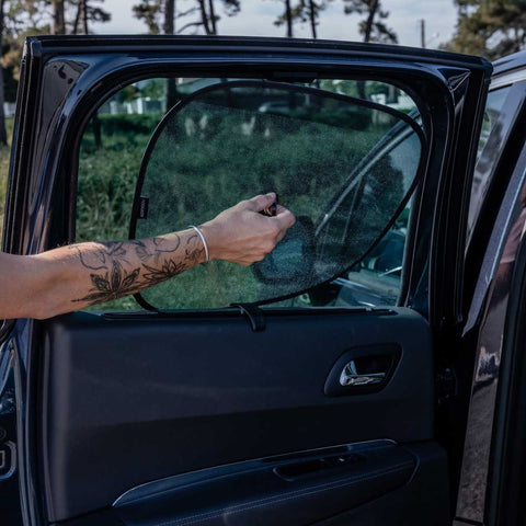 1. Person installing Ezimoov EZI SUN STOPPERS sun shade on car window outdoors