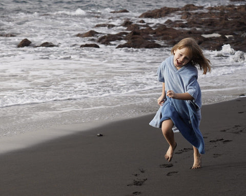 1. Child running on a beach wearing a blue bath poncho with hood, smiling, with ocean waves in the background