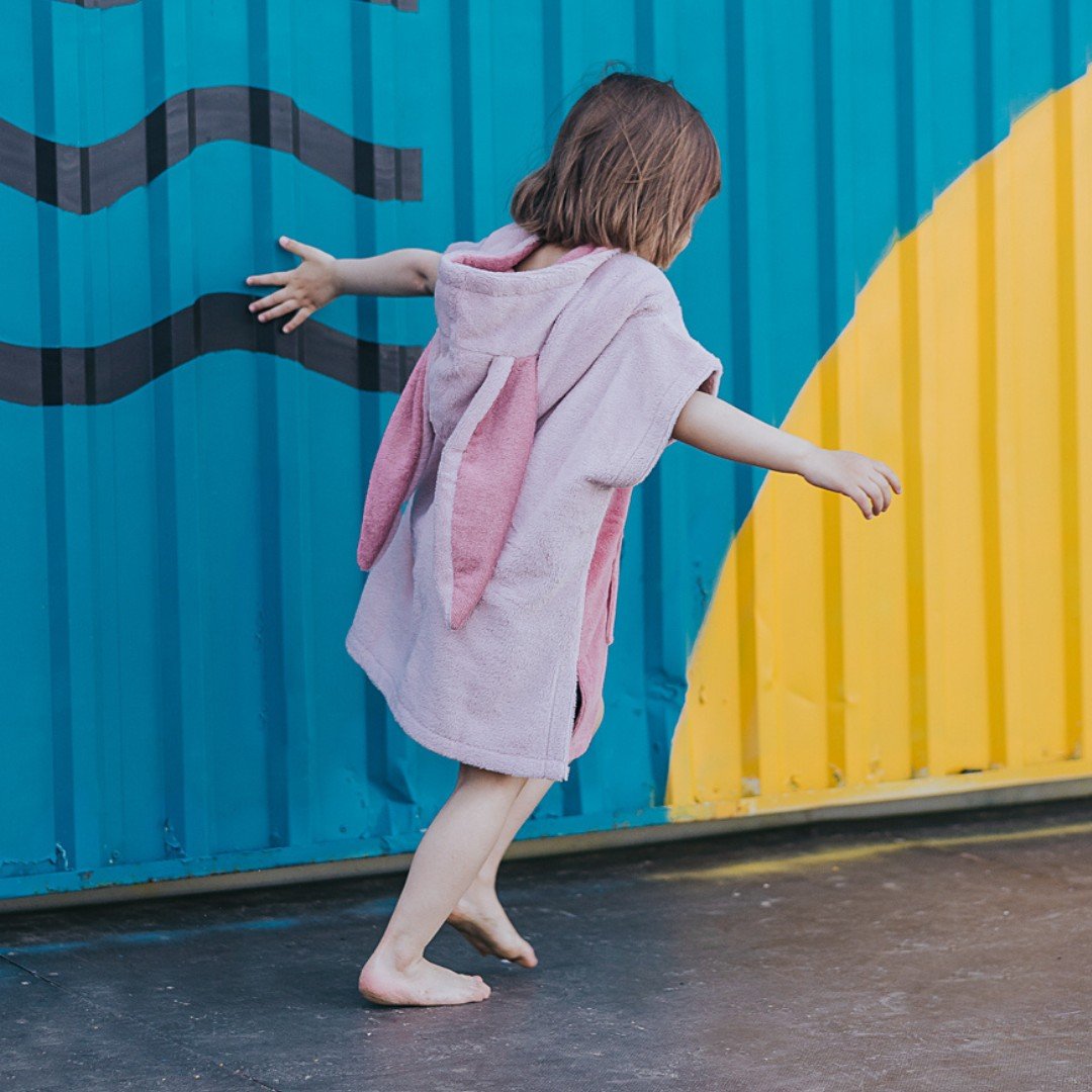 1. Child in pink Surfbunny bath poncho with bunny ears playing near colorful wall