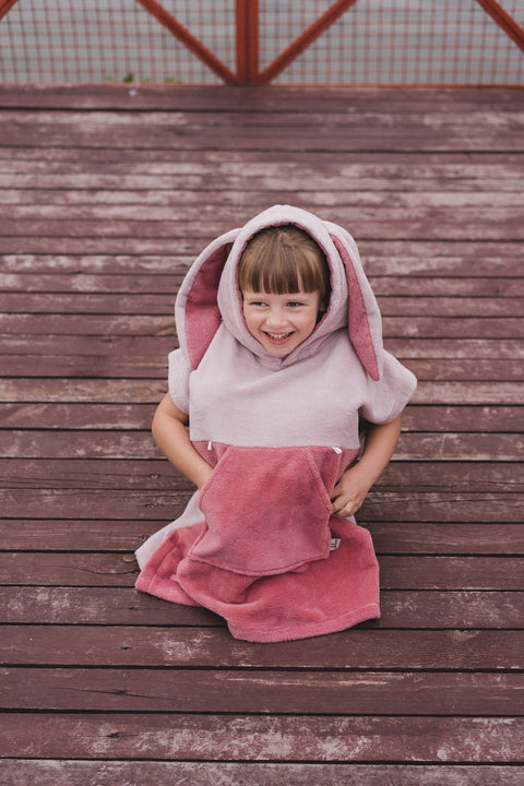 1. Child wearing pink Surfbunny bath poncho with bunny ears on a wooden deck
