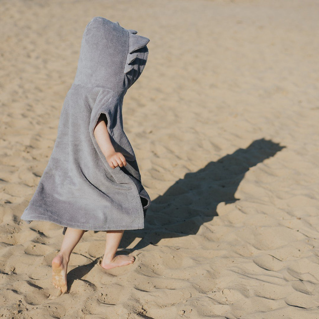 3. Child walking on sand wearing grey Surfdragon kids bath poncho with hood and ears, shown from back