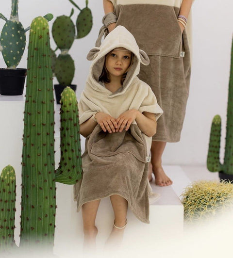 5. Child wearing beige Surfsheep kids bath poncho with hood and ears sitting among cacti
