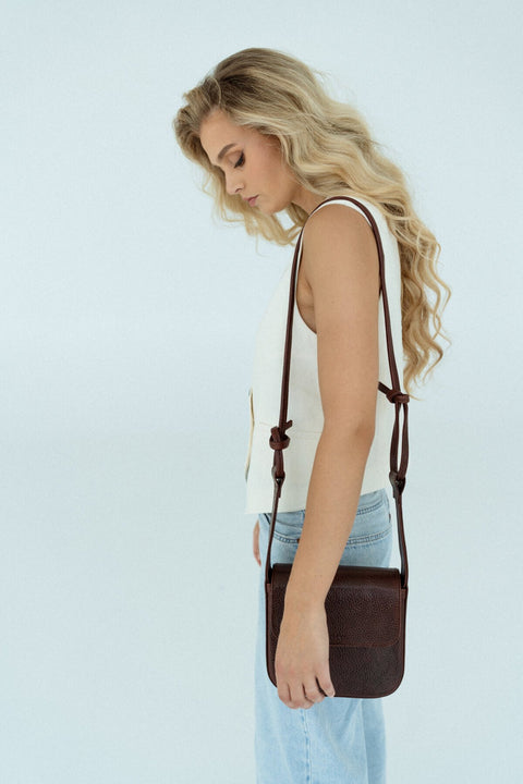 2. Side view of woman wearing brown MUSA crossbody bag by Lava Flow, highlighting sleek design and adjustable strap