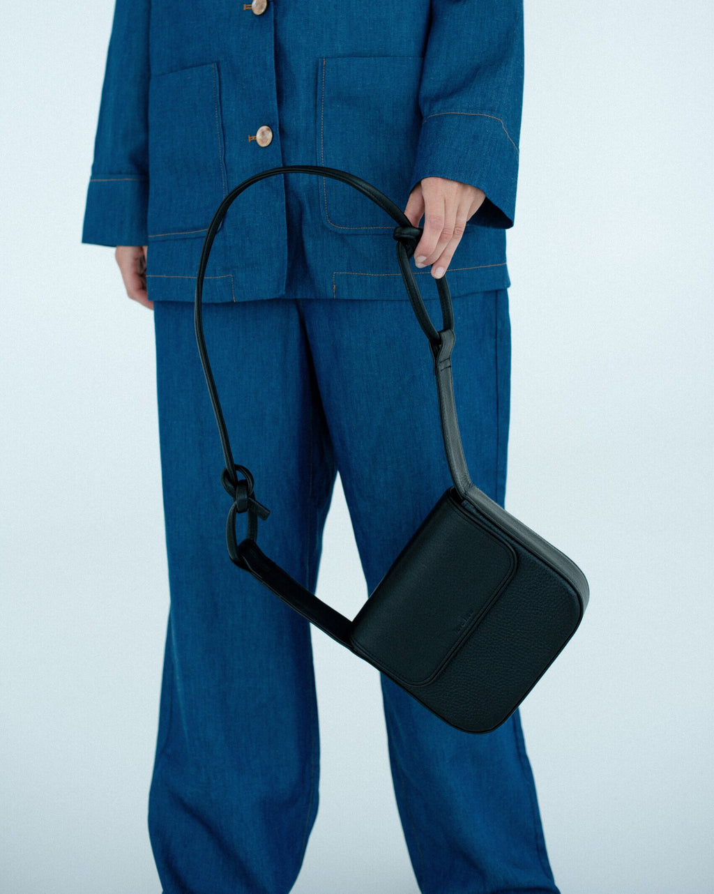 3. Black MUSA crossbody bag by Lava Flow, held by model in blue denim outfit, studio setting