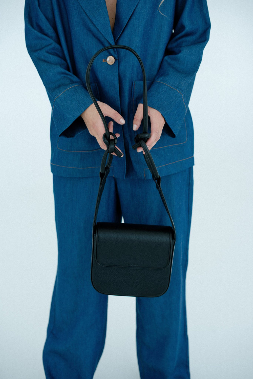 2. Women's black MUSA crossbody bag by Lava Flow, held by model in blue denim outfit, studio setting