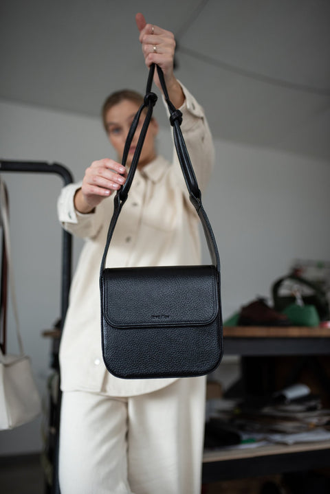 5. Black MUSA crossbody bag by Lava Flow, held by model in cream outfit, studio setting