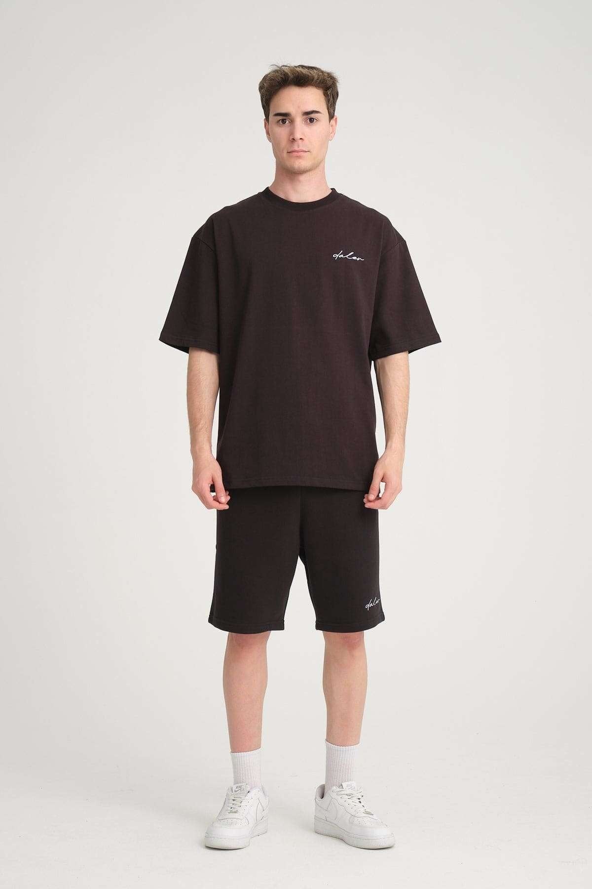 1. Man wearing black sweat shorts and matching t-shirt with white sneakers, standing in studio setting