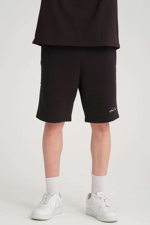 2. Front view of black sweat shorts worn by a man with white sneakers, showcasing fit and logo detail
