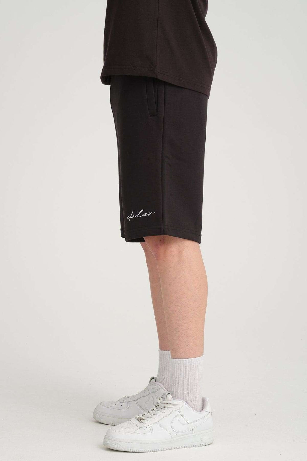 4. Side view of black sweat shorts worn by a man, highlighting side pocket and logo embroidery