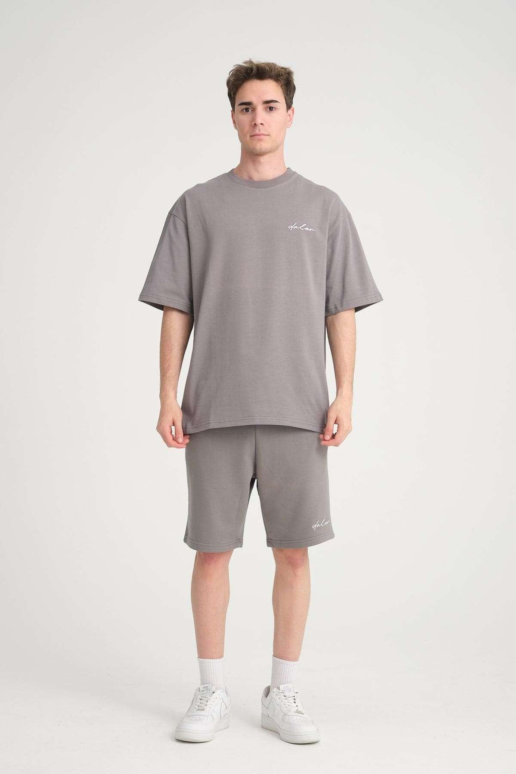 1. Man in grey oversized t-shirt and matching sweat shorts with logo, standing in studio