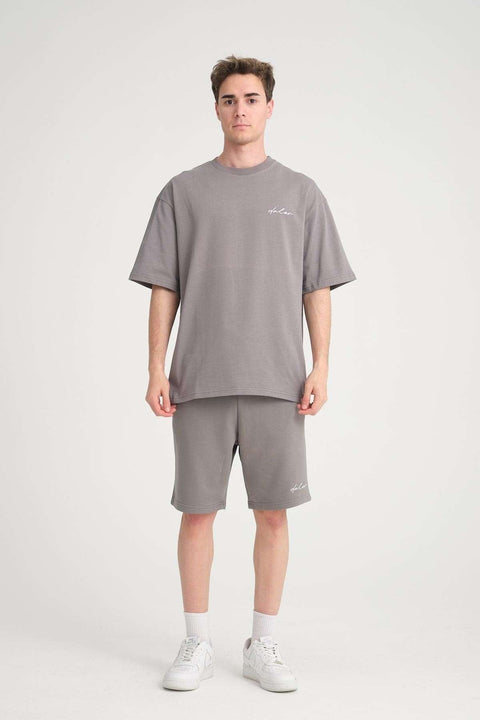 1. Man in grey oversized t-shirt and matching sweat shorts with logo, standing in studio