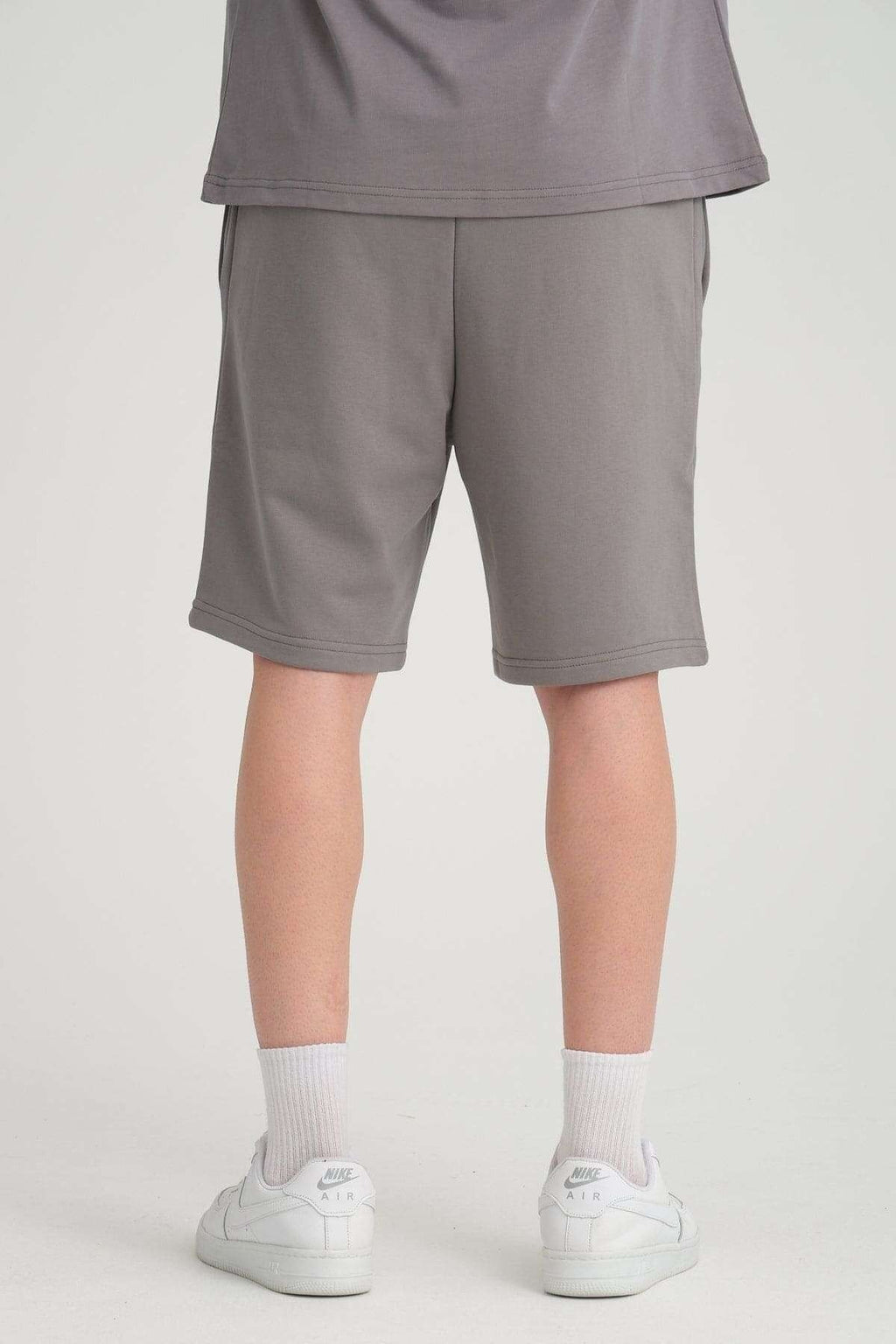 2. Back view of grey sweat shorts with elastic waistband, worn with white sneakers in studio setting