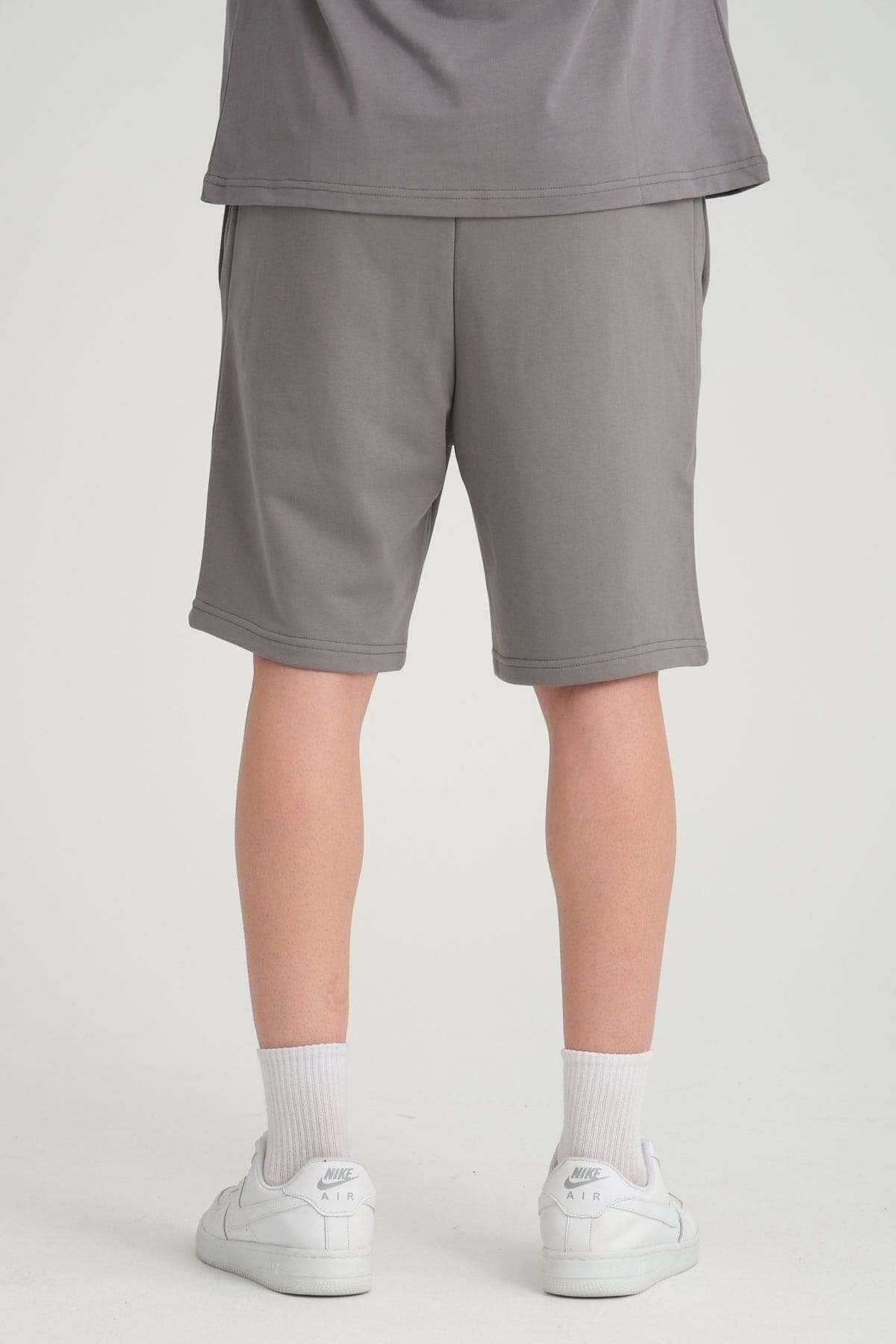 2. Back view of grey sweat shorts with elastic waistband, worn with white sneakers in studio setting