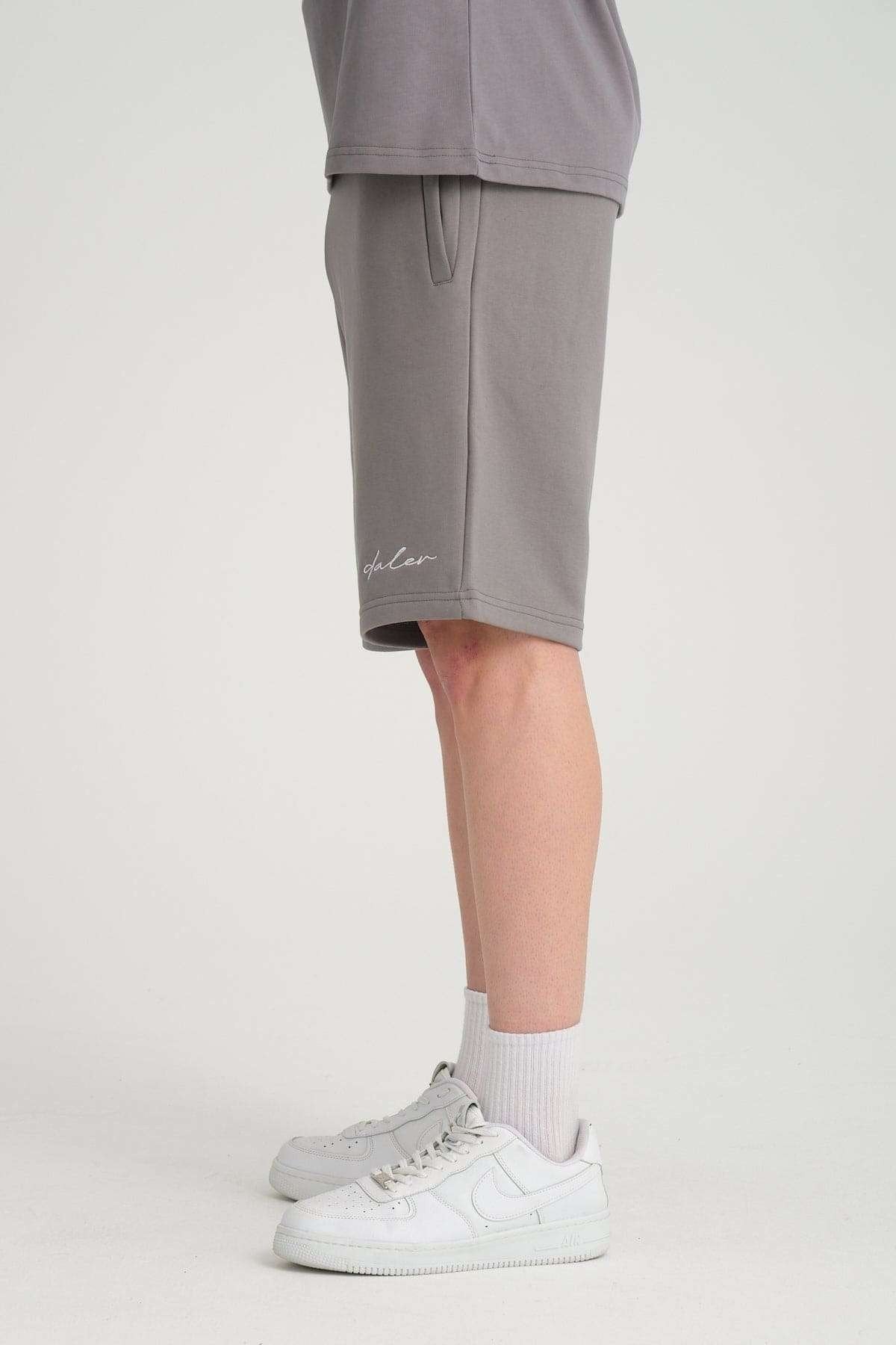 2. Side view of grey sweat shorts with logo embroidery and elastic waistband, worn with white sneakers