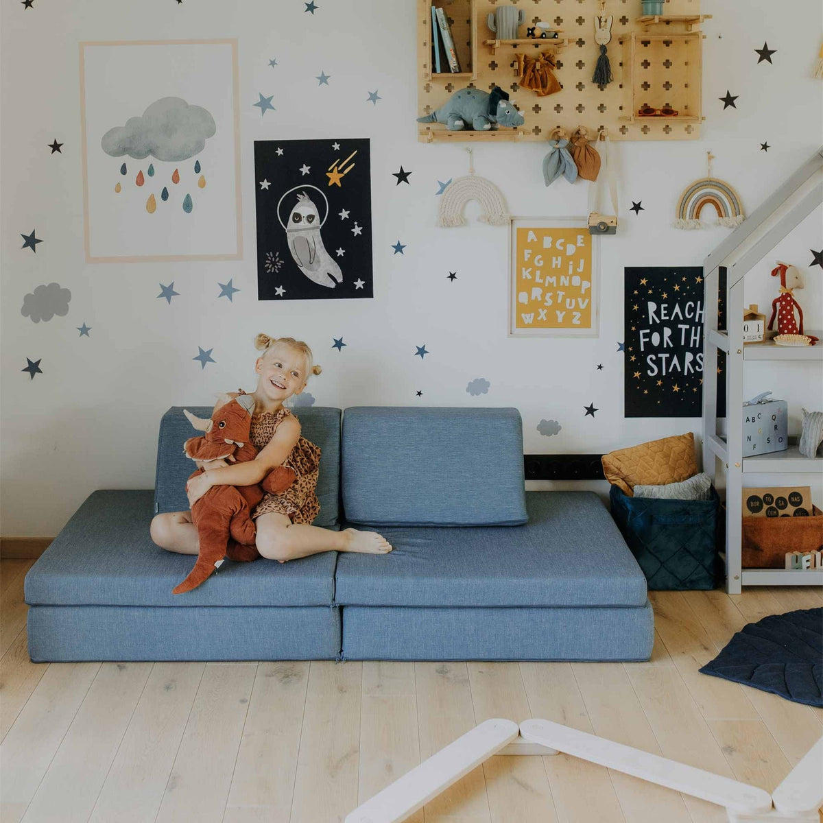 2. Girl sitting on turquoise Monboxy play mattress sofa holding a stuffed toy in a star-themed children's room