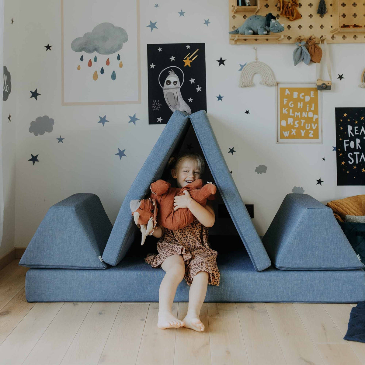 8. Girl sitting inside a tent made from turquoise Monboxy play mattress set in a star-themed children's room