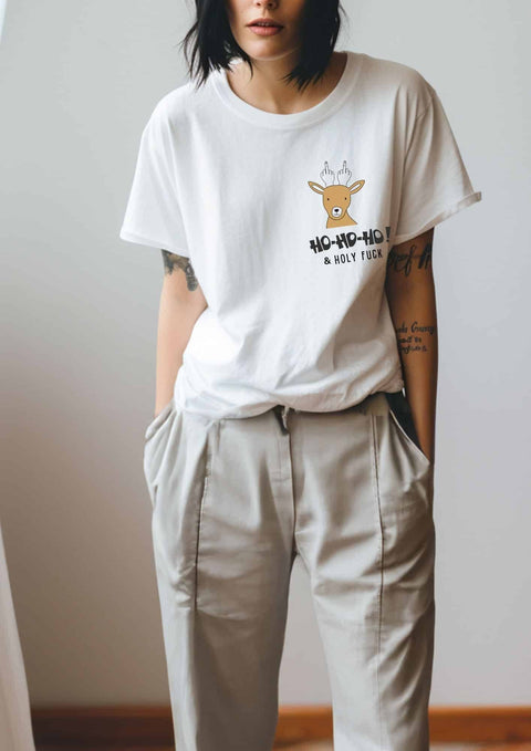 2. Woman in white Black Giraffe Brand T-shirt with reindeer graphic and 'Ho-ho-ho! & Holy Fuck' text, paired with beige pants in relaxed pose