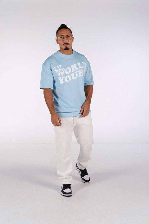 3. Man in baby blue oversized t-shirt with 'The World Is Yours' print, wearing white pants and sneakers in studio