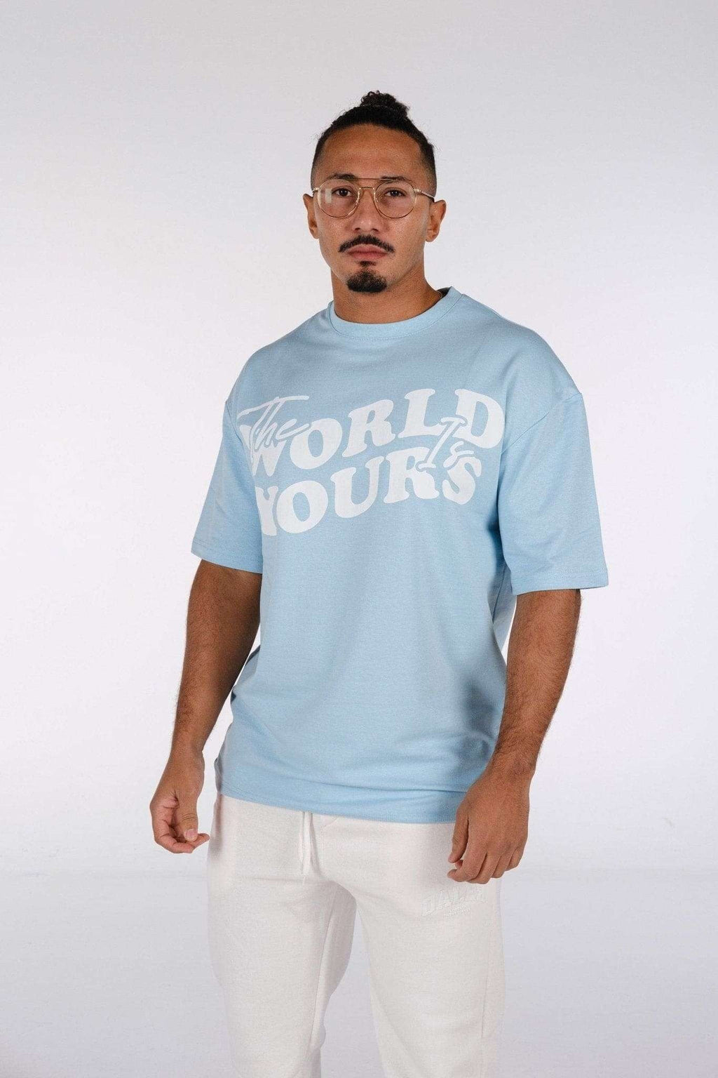 2. Man wearing baby blue oversized t-shirt with 'The World Is Yours' print, paired with white pants in studio