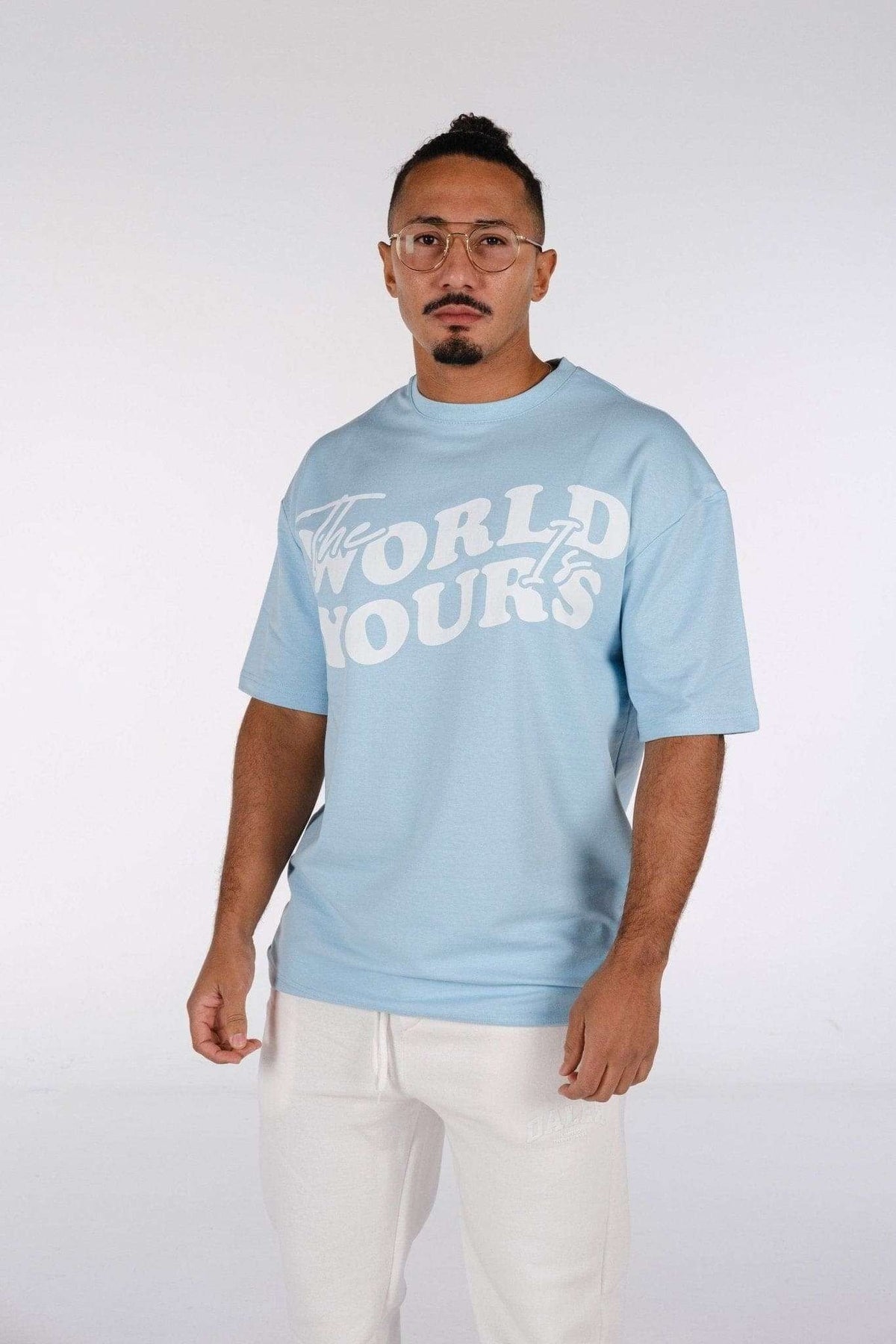 2. Man wearing baby blue oversized t-shirt with 'The World Is Yours' print, paired with white pants in studio