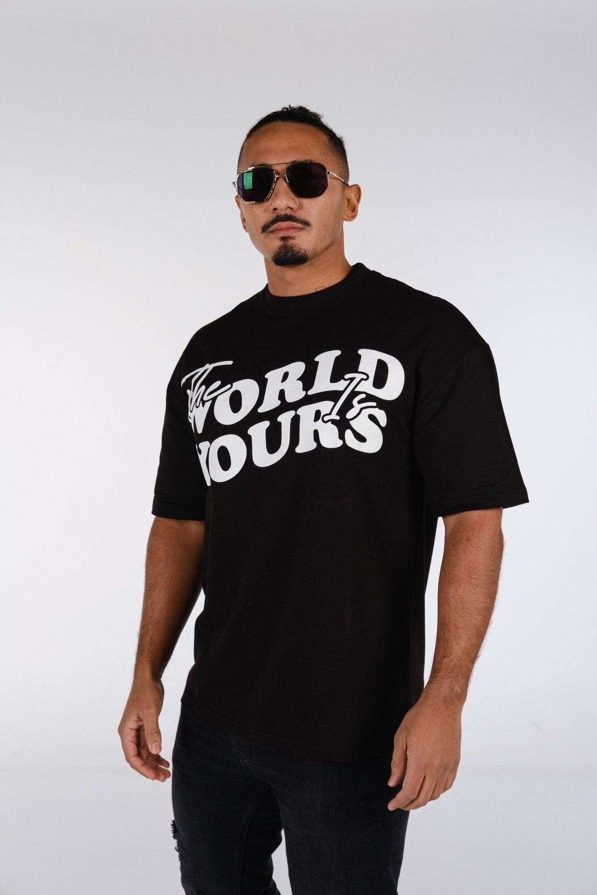 3. Man wearing oversized black t-shirt with 'The World Is Yours' print, styled with sunglasses, in studio