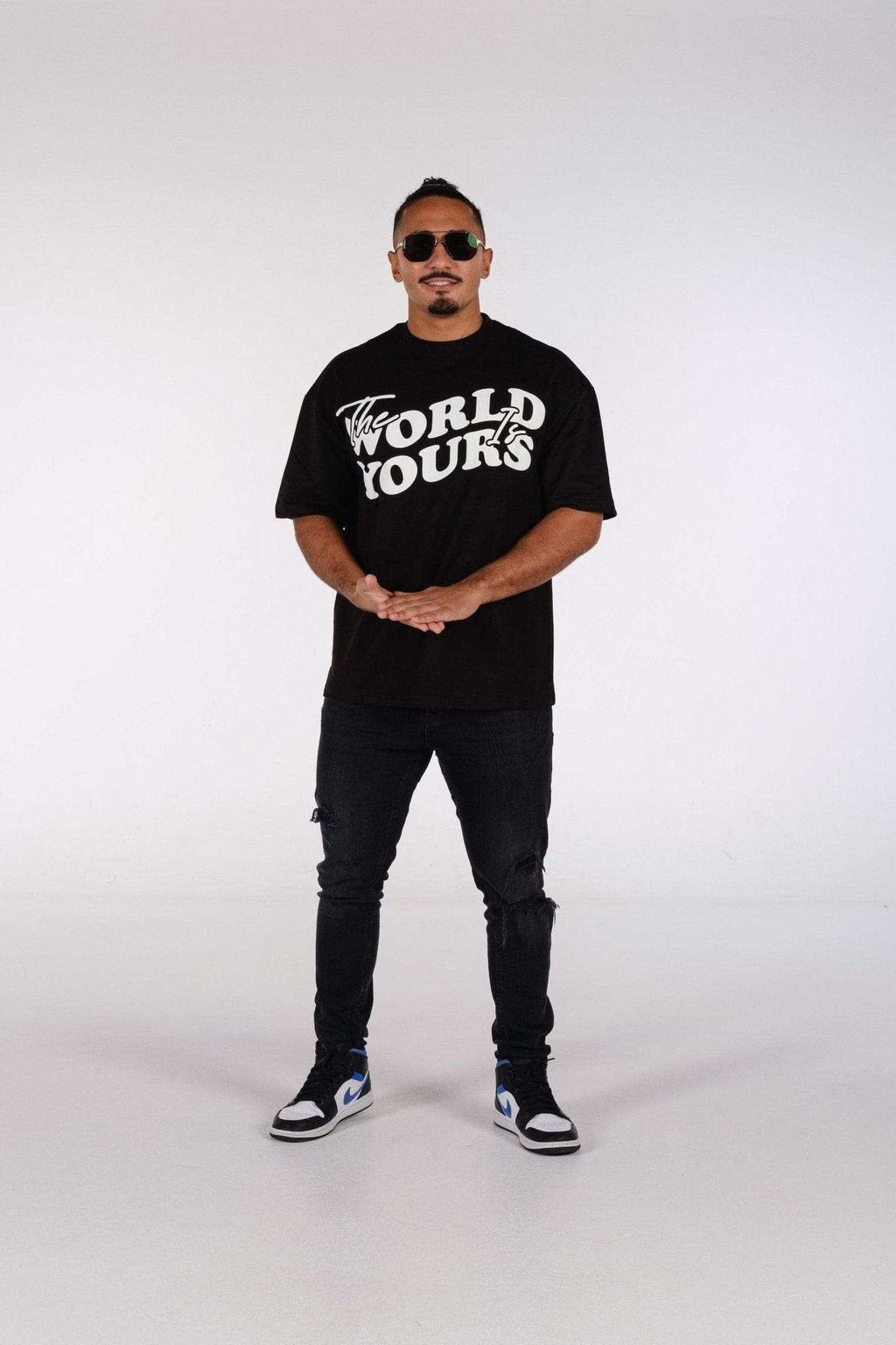 4. Man in oversized black t-shirt with 'The World Is Yours' print, wearing jeans and sneakers, standing in studio
