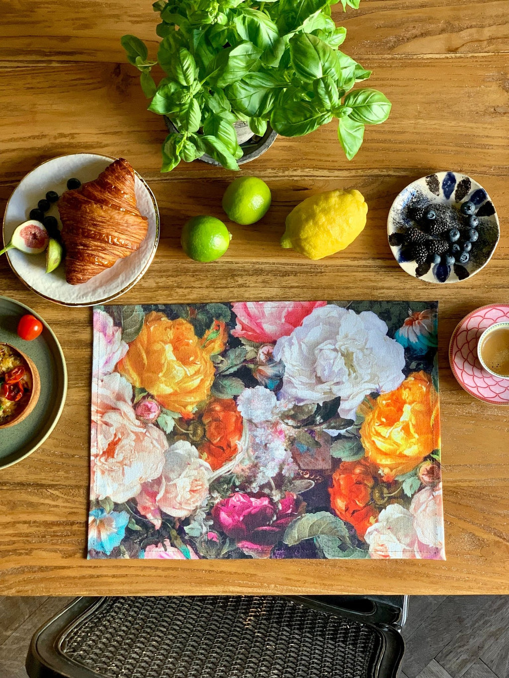 1. Floral printed cotton placemat on wooden table with croissant, fruit, and coffee, enhancing a vibrant breakfast setting