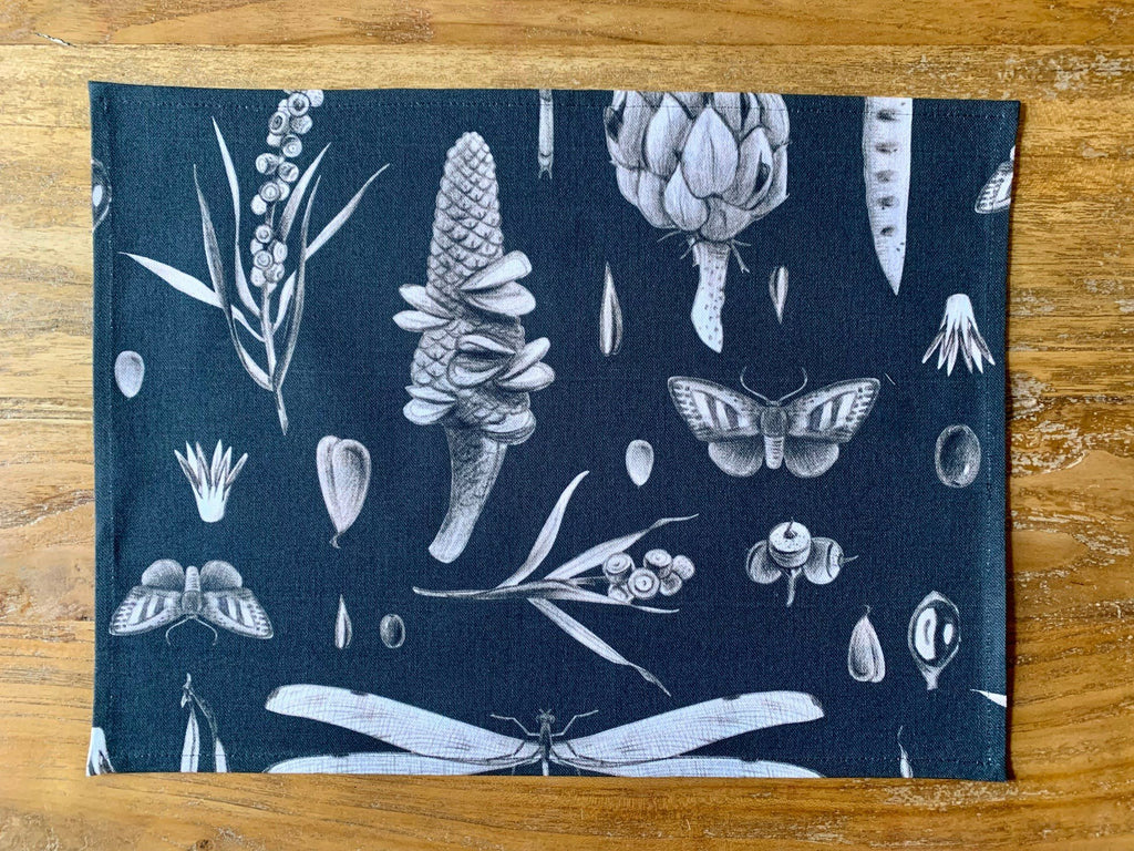 2. Studio shot of black Seeds Carbon print cotton placemat by Hortensias Home featuring botanical and insect illustrations