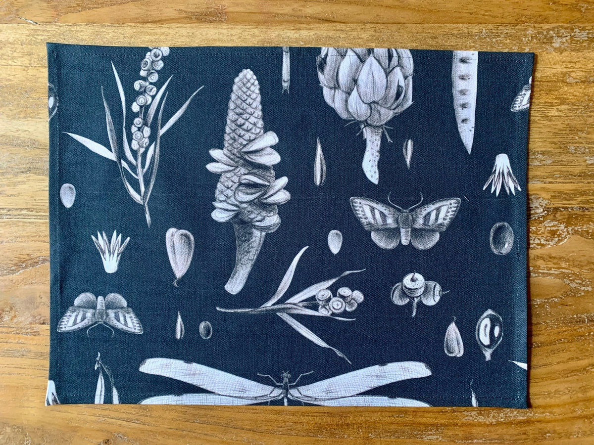 2. Studio shot of black Seeds Carbon print cotton placemat by Hortensias Home featuring botanical and insect illustrations