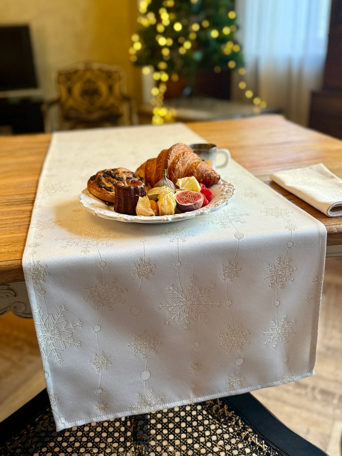 1. Golden Snowfall table runner by Hortensias Home on wooden table with festive pastries and coffee, Christmas tree in background
