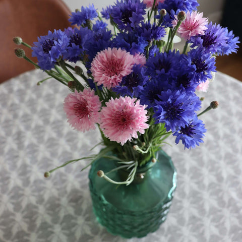 2. Close-up of LOKO Hanikatsi Fly tablecloth in beige with Hiiumaa mitten pattern, topped with a green vase holding pink and blue flowers