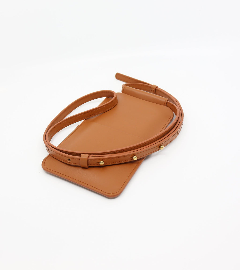 6. Flat lay of Tairi Roosve tan leather phone bag with adjustable strap and Sam Browne buttons