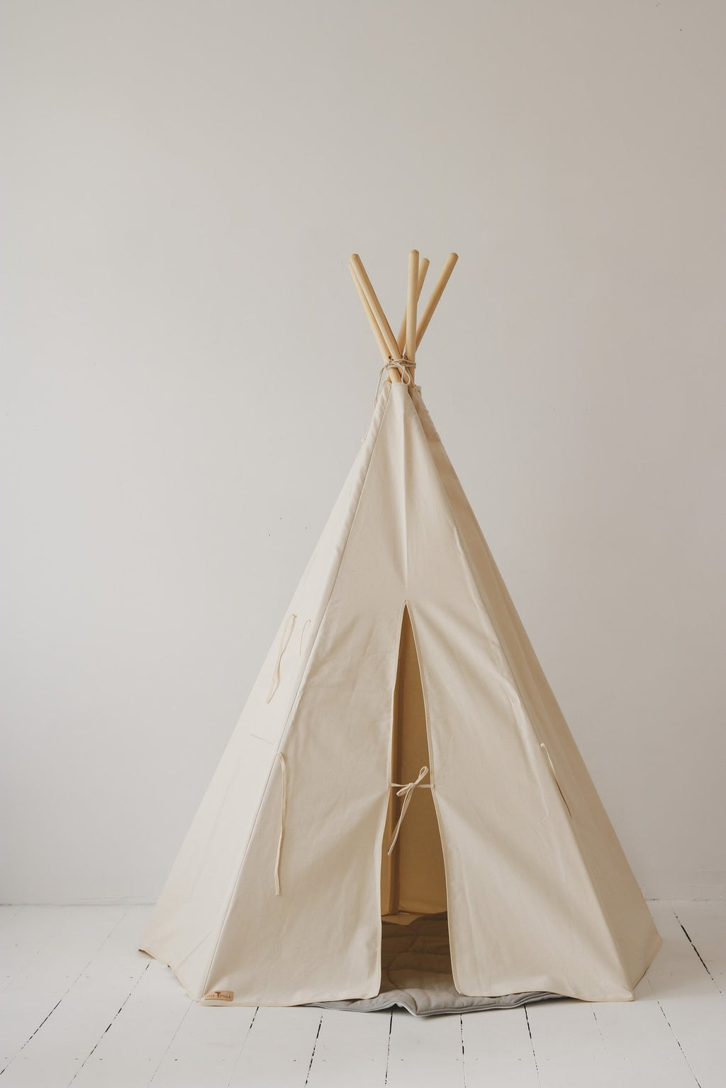 2. Beige teepee tent with closed entrance, made from cotton and pine poles, in a studio setting