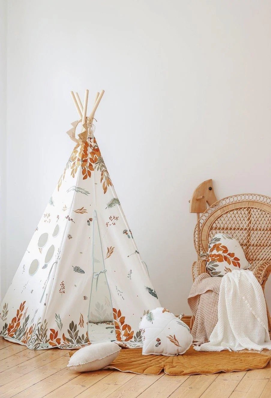 3. Indoor setup of children's teepee tent with forest pattern, next to wicker chair and cushions