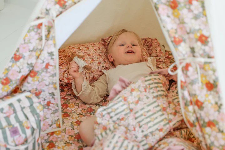 1. Child lying inside Moi Mili Green Garden teepee tent with floral print, surrounded by matching cushions