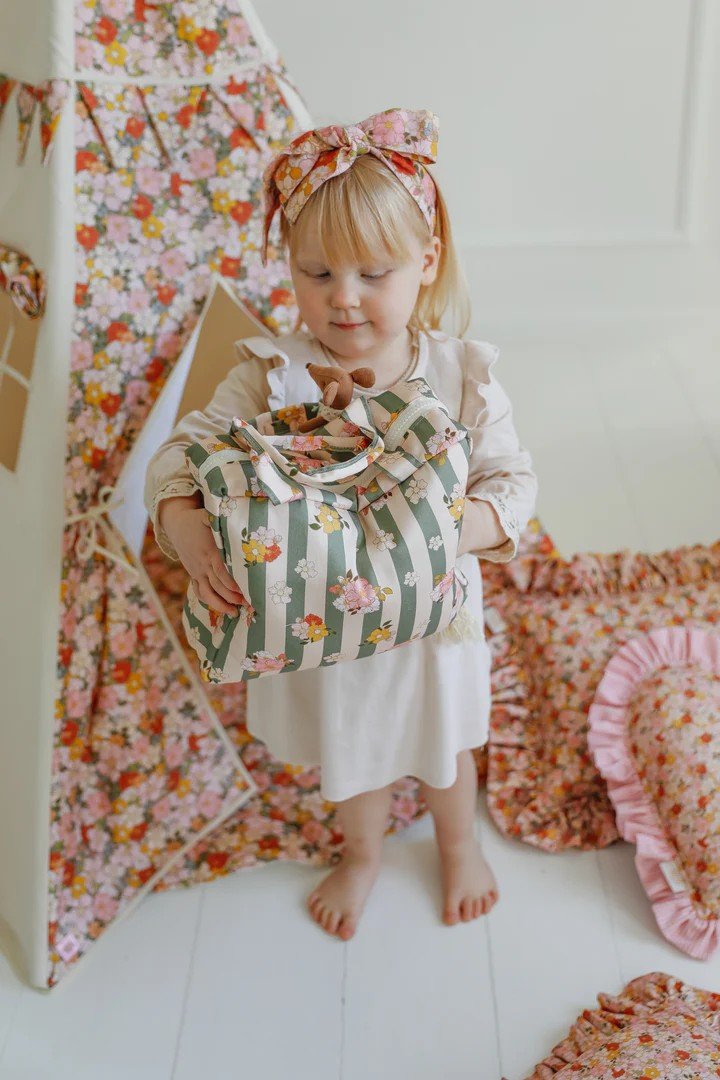 1. Child holding a striped floral bag next to Moi Mili Green Garden teepee tent with floral print