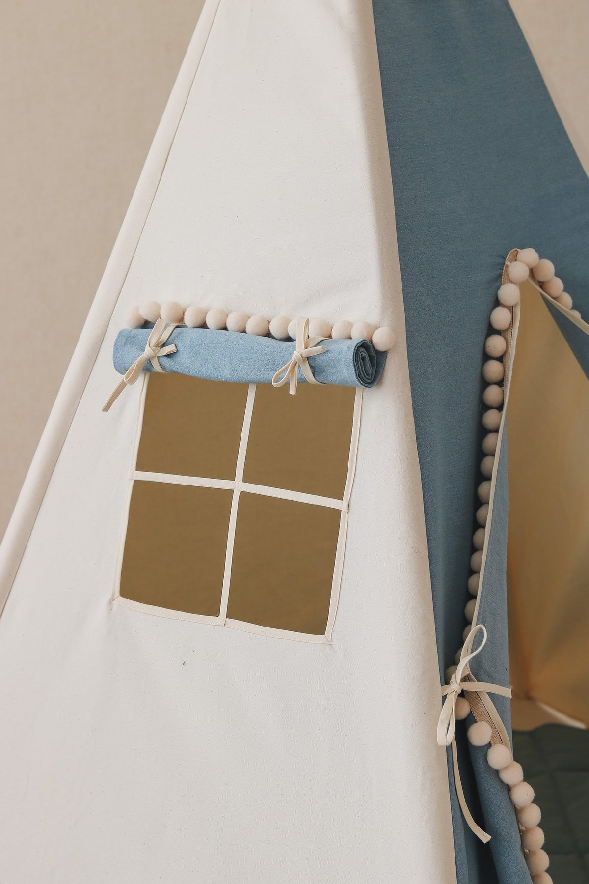 5. Close-up of blue and white teepee tent window with rolled curtain and pompoms, highlighting fabric detail.