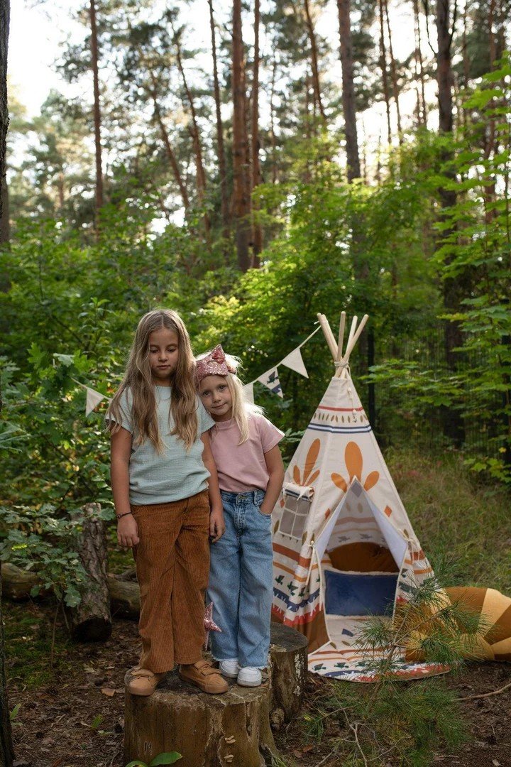 1. Two girls standing beside a teepee tent with Native Vibe print in a forest setting
