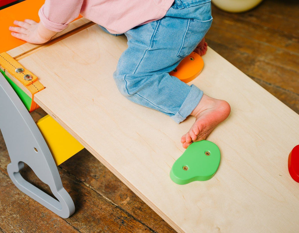 2. Child climbing on Sway Rainbow Ramp with colorful rocks, wearing jeans and pink top
