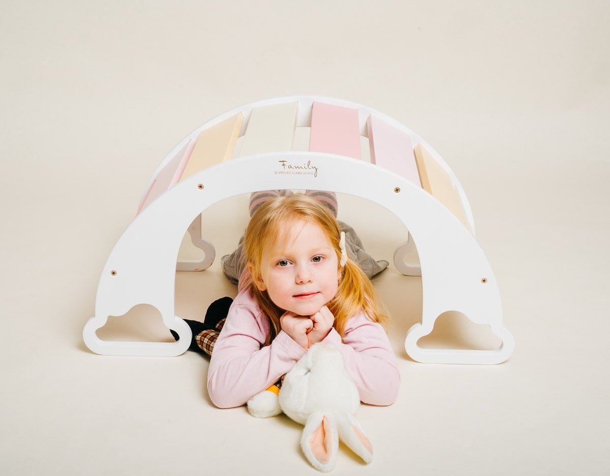 1. Child lying under colorful rainbow climber with a stuffed toy