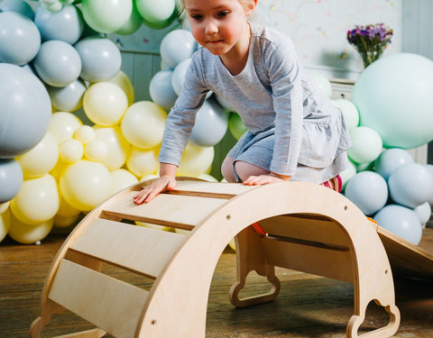 1. Child climbing over natural finish rainbow climber with colorful balloons in background