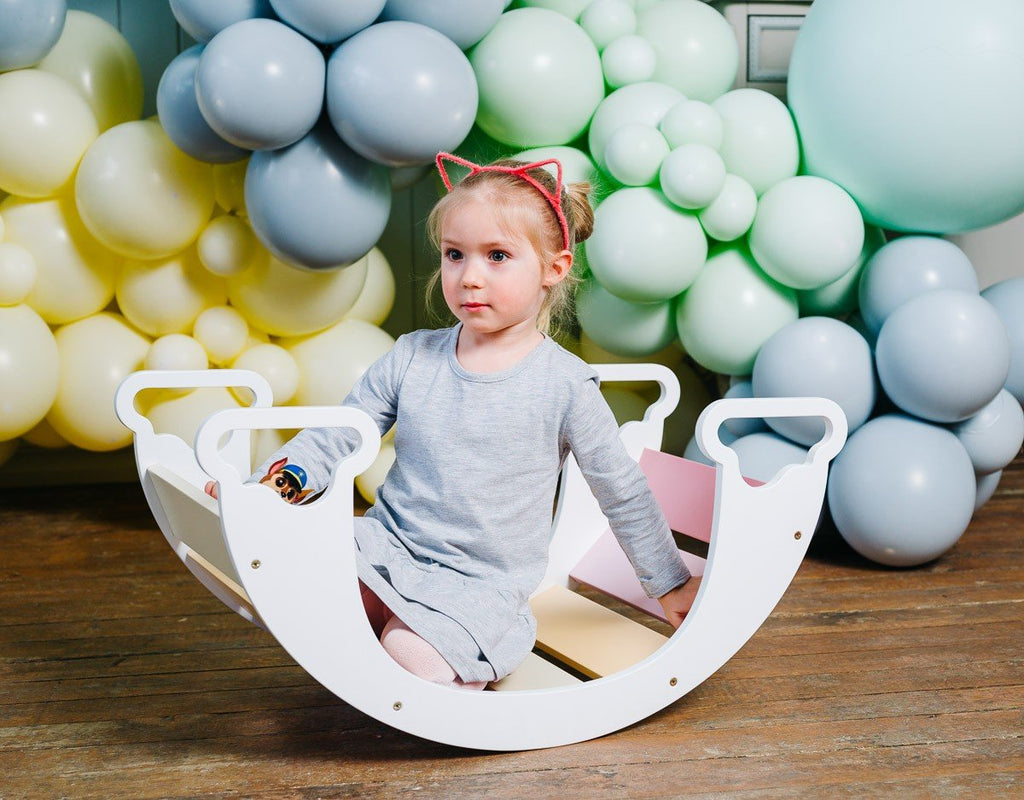 1. Child sitting inside colorful rainbow climber with balloons in background