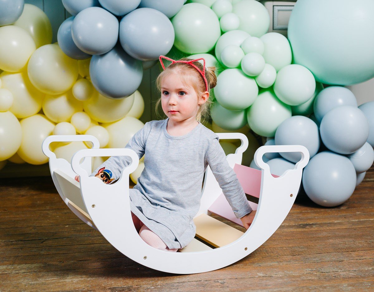 1. Child sitting inside colorful rainbow climber with balloons in background